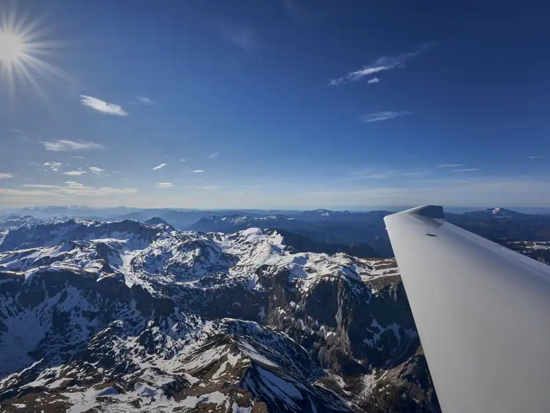Blick über die Tragfläche auf die verschneiten Alpengipfel bei einem winterlichen Rundflug