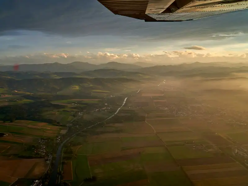 Rundflug über ein Flusstal mit Feldern und Dörfern im warmen Abendlicht