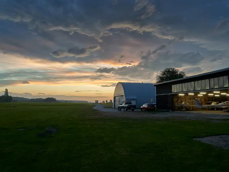 Beleuchteter Hangar am Flugplatz Völtendorf in der Abenddämmerung mit abgestellten Flugzeugen