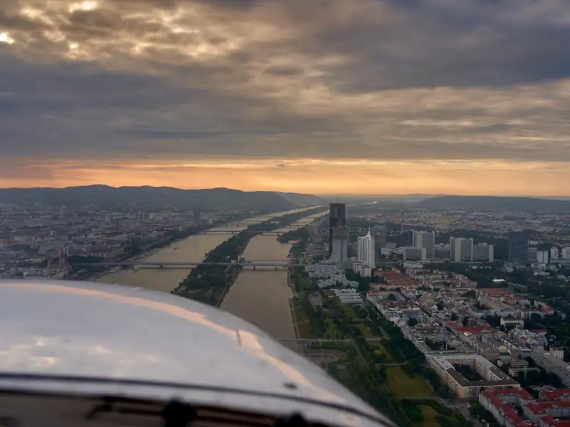 Rundflug über Wien: Blick entlang der Donau auf die Skyline in der Abenddämmerung